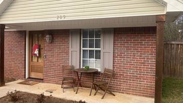 Une maison en briques avec un porche, le numéro « 209 » au-dessus de la porte, et une petite table avec des chaises.