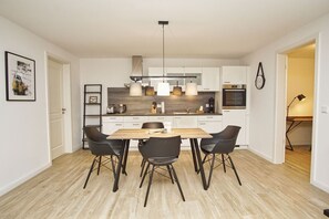 A modern kitchen with white cabinets, a wooden dining table, and black chairs. - Close to the sailing harbor - Alte Fischfabrik Lauterbach FeWo 07 RELAXEN in Lauterbach (Putbus)