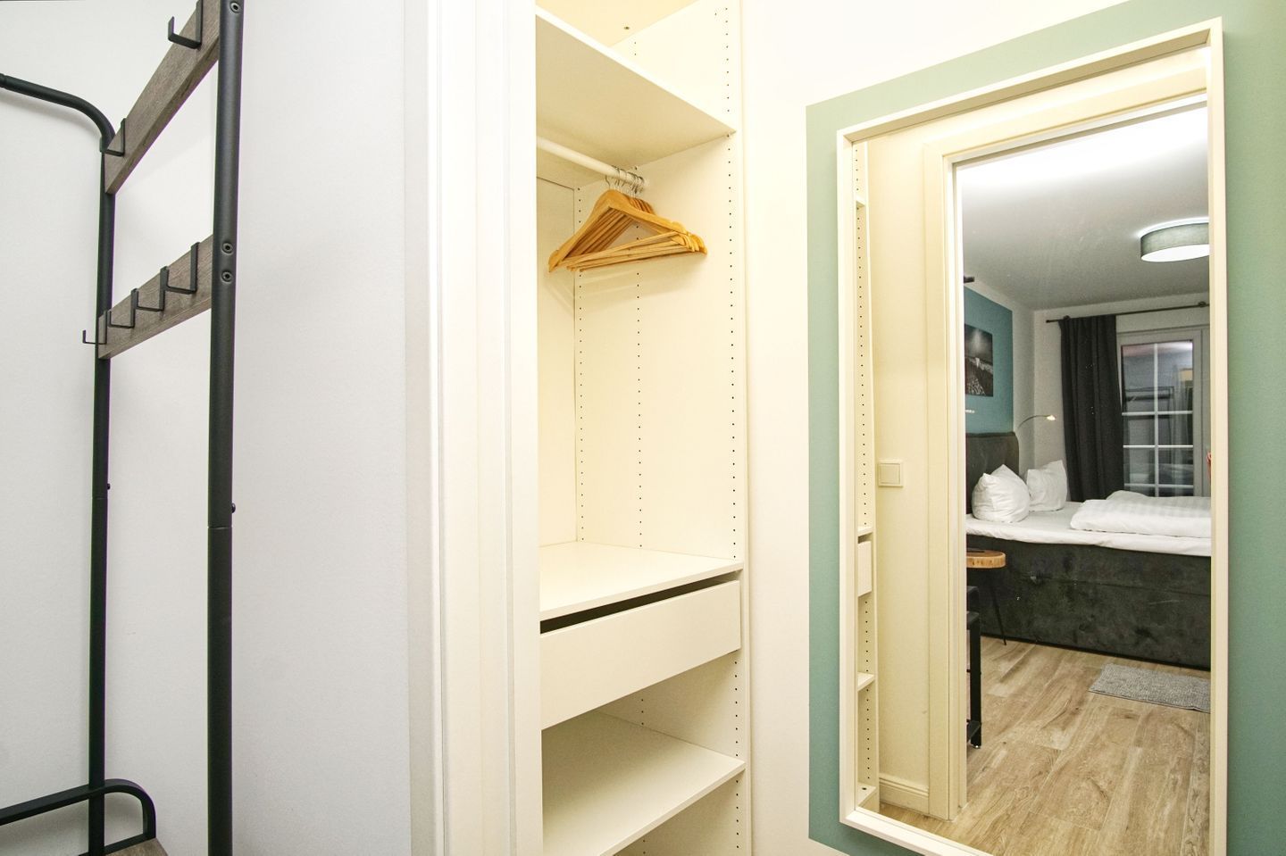 A hotel room with a walk-in closet, a bed, a bathroom with a mirror, and a wooden floor.
