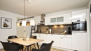 Uma cozinha moderna com armários brancos, uma mesa de jantar de madeira e cadeiras pretas.