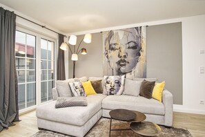 A modern living room with a grey sectional sofa, a small round coffee table, and a large abstract painting on the wall. - Close to the sailing harbor - Alte Fischfabrik Lauterbach FeWo 07 RELAXEN in Lauterbach (Putbus)