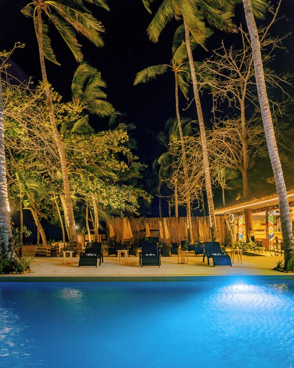 A nighttime pool area with palm trees, lounge chairs, and a bar area. - THE DOME RESORTS, INC. (Puerto Princesa)