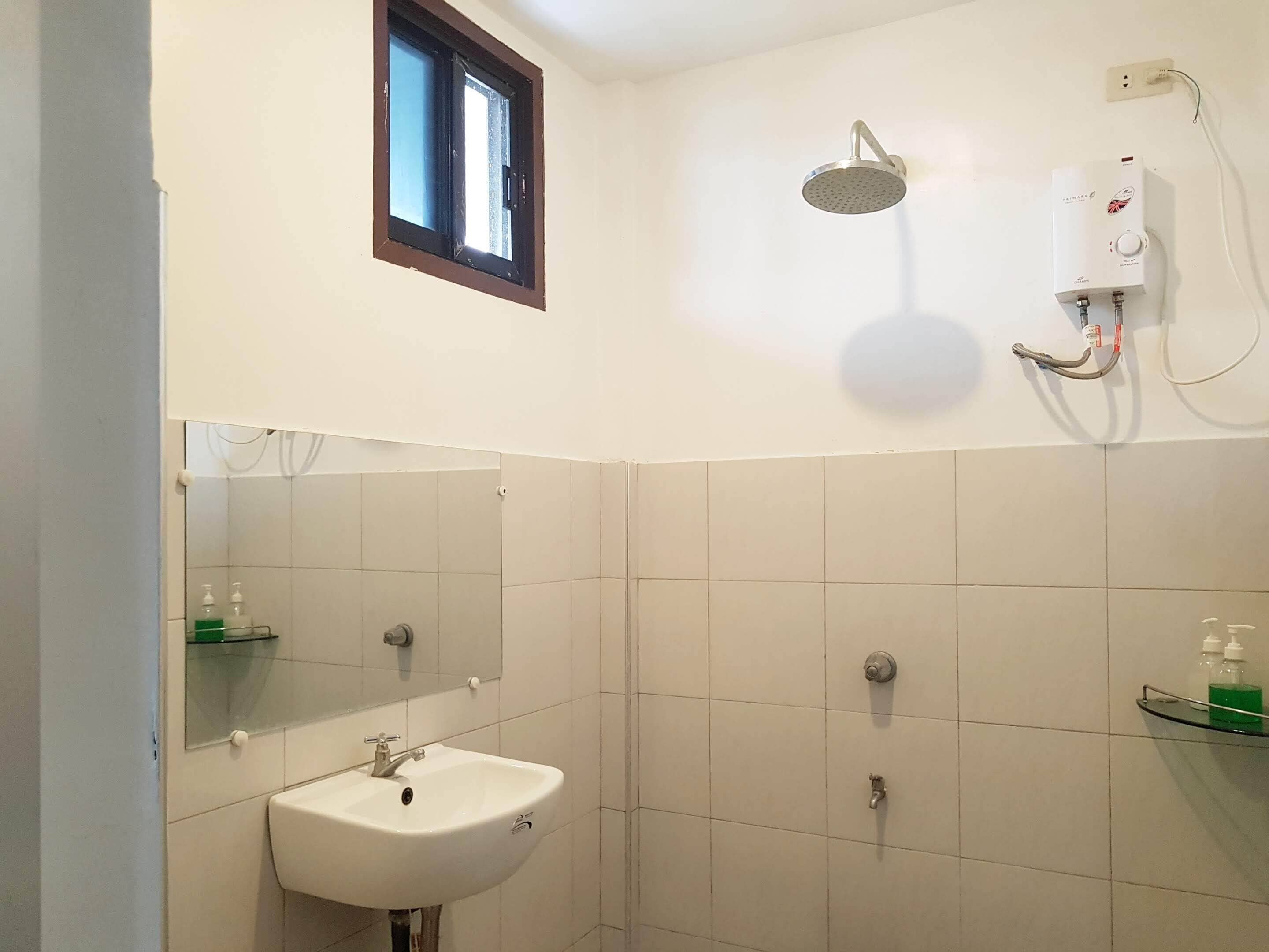 Ein Badezimmer mit einem weißen Waschbecken, einem Spiegel, einer Dusche und einem Fenster.