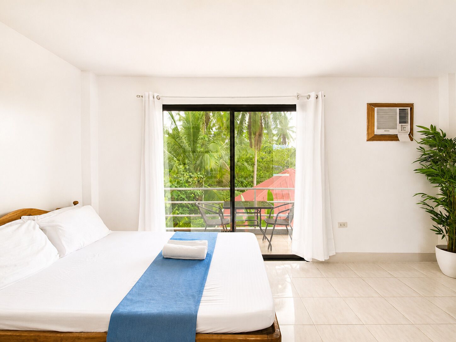 A hotel room with a bed, a balcony with a table and chairs, and a potted plant.