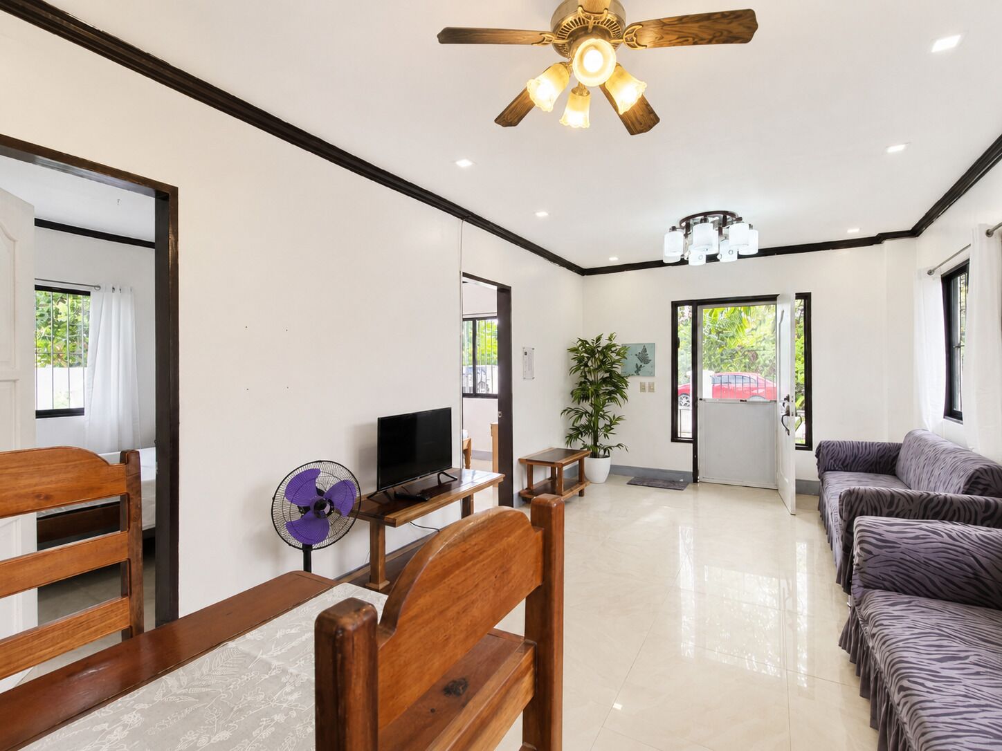A spacious room with a ceiling fan, a television, a wooden chair, a sofa, and a potted plant.