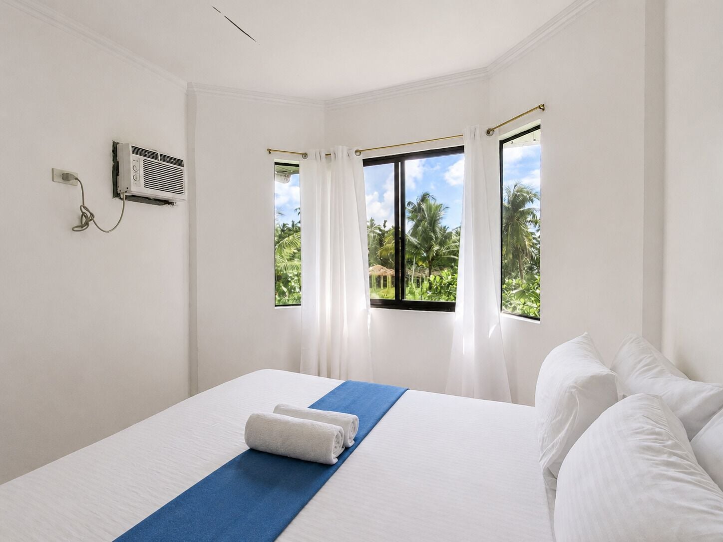 Habitación de hotel con cama, ventana con cortinas, aire acondicionado de pared y vista a zonas verdes.