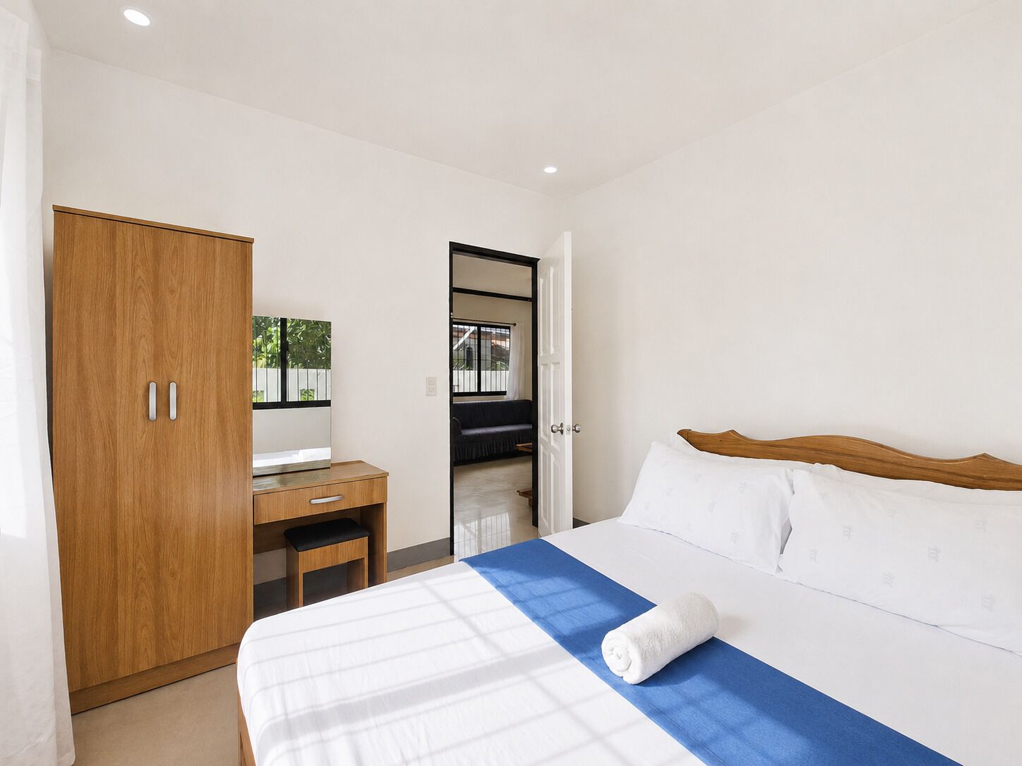 A bedroom with a bed, a wooden wardrobe, a desk, and a mirror.