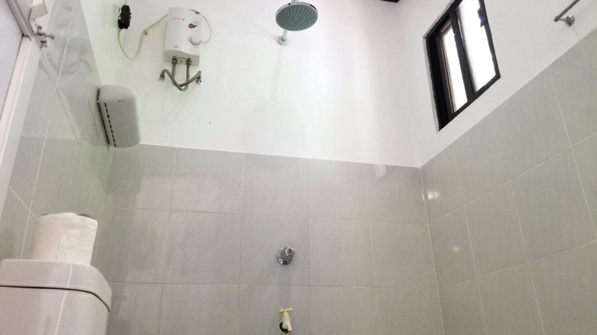 A bathroom with a shower, a toilet, and a towel dispenser.