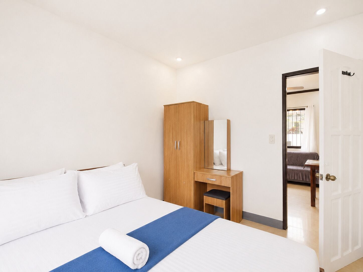 A hotel room with a bed, a wooden wardrobe, a mirror, and a door leading to another room.