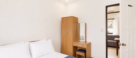 Habitación de hotel con cama, un armario de madera, un espejo y una puerta que da a otra habitación.
