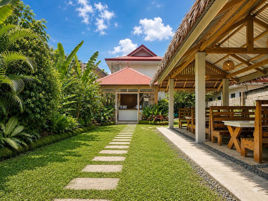 A tropical resort with a paved pathway leading to a covered outdoor seating area.