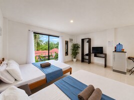 Habitación de hotel con una cama, un escritorio con televisor, una planta y vistas a palmeras.