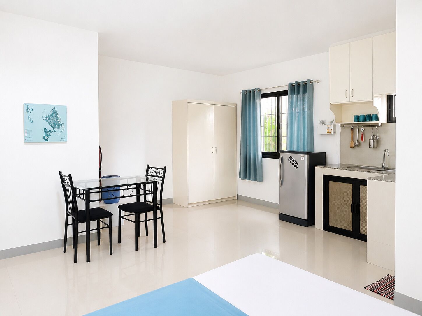 A compact kitchen with a dining table, chairs, a refrigerator, and a window with curtains.