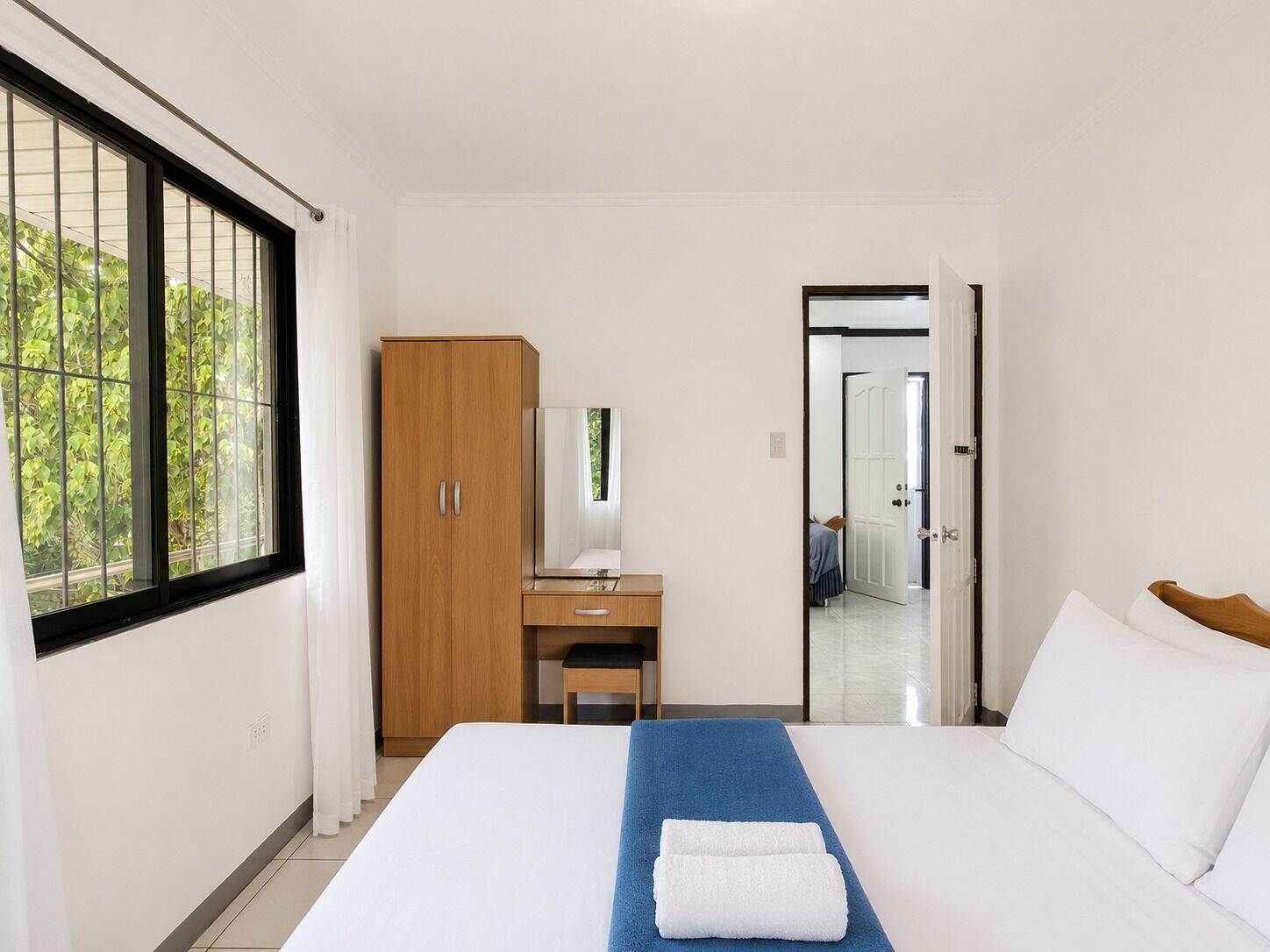 A hotel room with a bed, a desk, a wardrobe, and a view of greenery through the window.