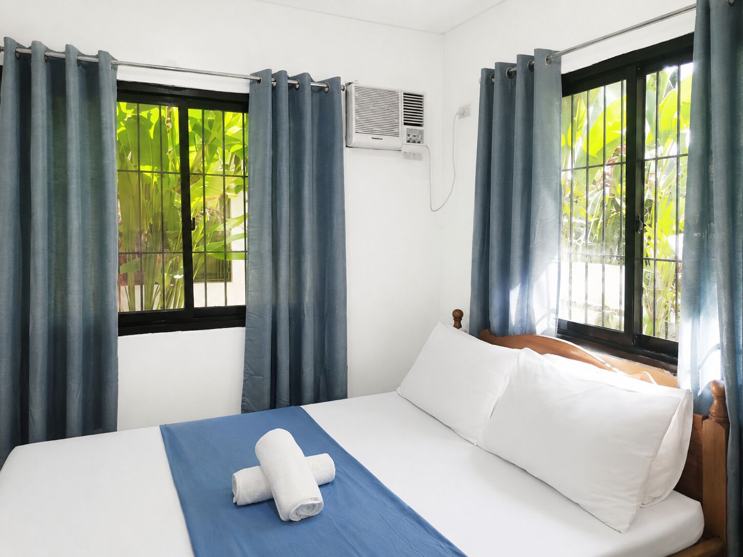 Habitación de hotel con cama, cortinas, aire acondicionado y ventana con vista a follaje.