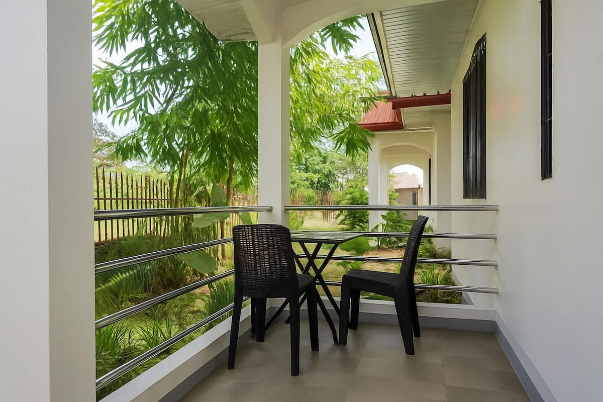 A balcony with two chairs and a table, overlooking a garden with trees and a fence.