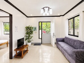 A modern living room with a sofa, a TV, a wooden table, a potted plant, and a door leading to an outdoor area. - Yayay Siargao (General Luna)