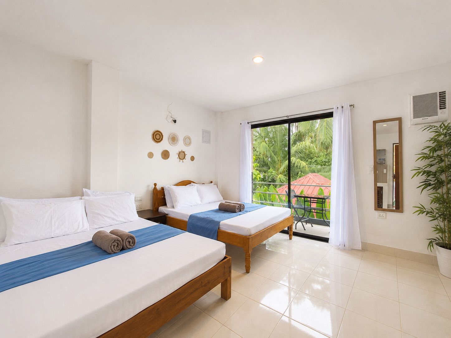 A hotel room with two beds, a large window with a view of greenery, a mirror, and a potted plant.