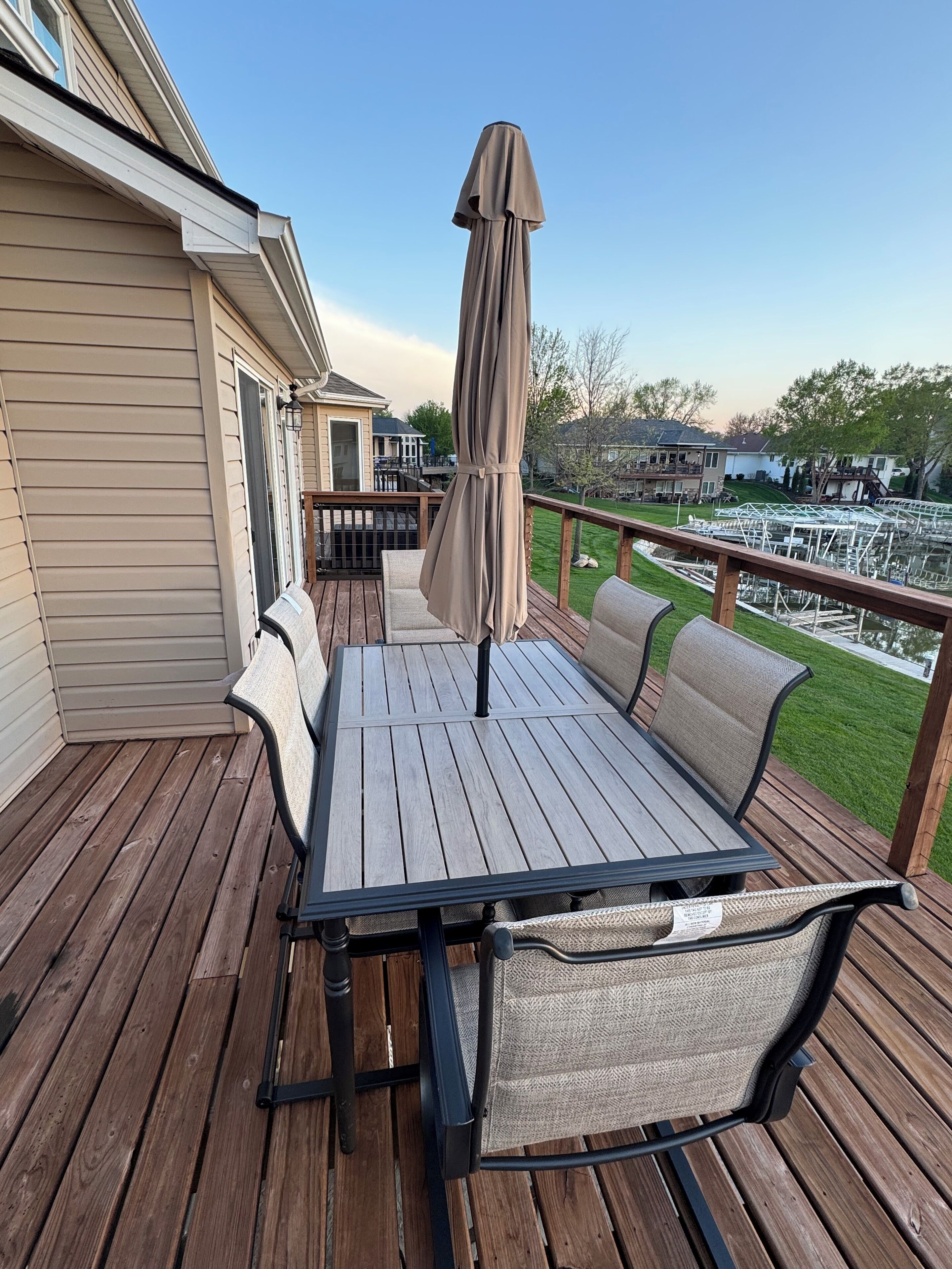 A wooden deck with a table and chairs, a covered umbrella, and a view of a residential area.