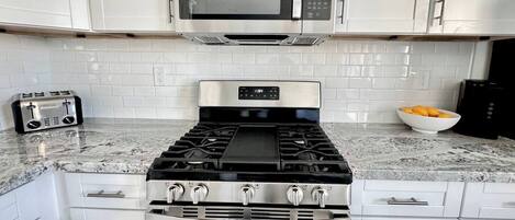 A kitchen with white cabinets, a stainless steel stove, a microwave, a toaster, and a bowl of fruit on the counter.