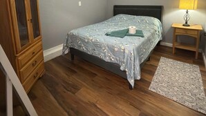 Une chambre à coucher comprenant un lit, un ventilateur de plafond, une commode en bois et une lampe de chevet.