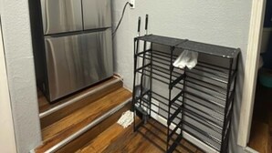 Une cuisine dotée d’un réfrigérateur en acier inoxydable, d’une étagère en métal noir et d’un plancher en bois.