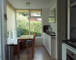 Ett kompakt kök med ett matbord och stolar, en inbyggd ugn och utsikt över grönområden utanför.