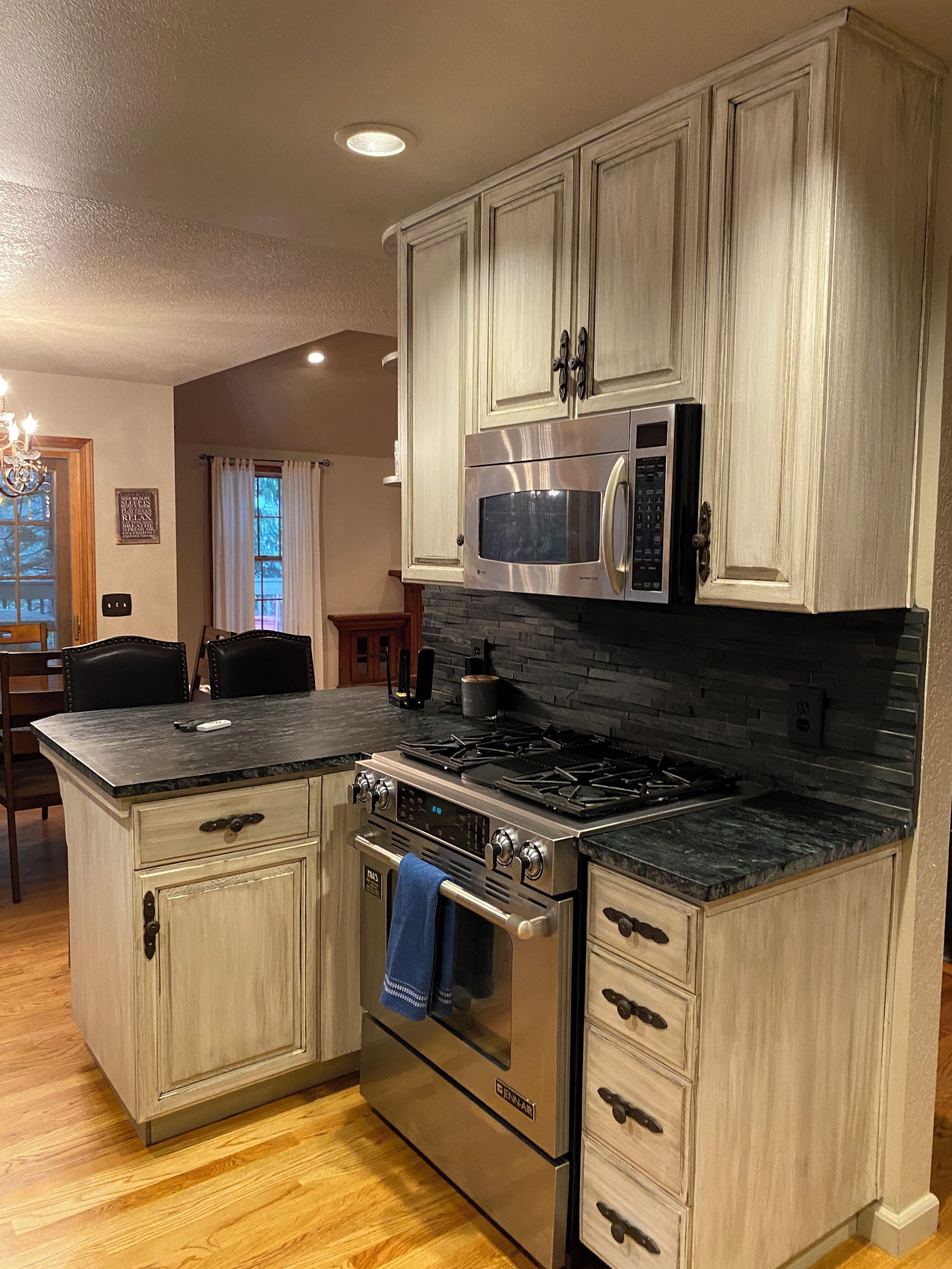 Una cocina con armarios de madera clara, estufa de acero inoxidable, microondas y salpicadero de piedra.