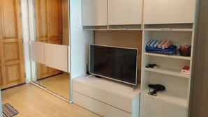 Ein modernes Zimmer mit Fernseher, Holzschrank und weißem Schrank mit Regalen.