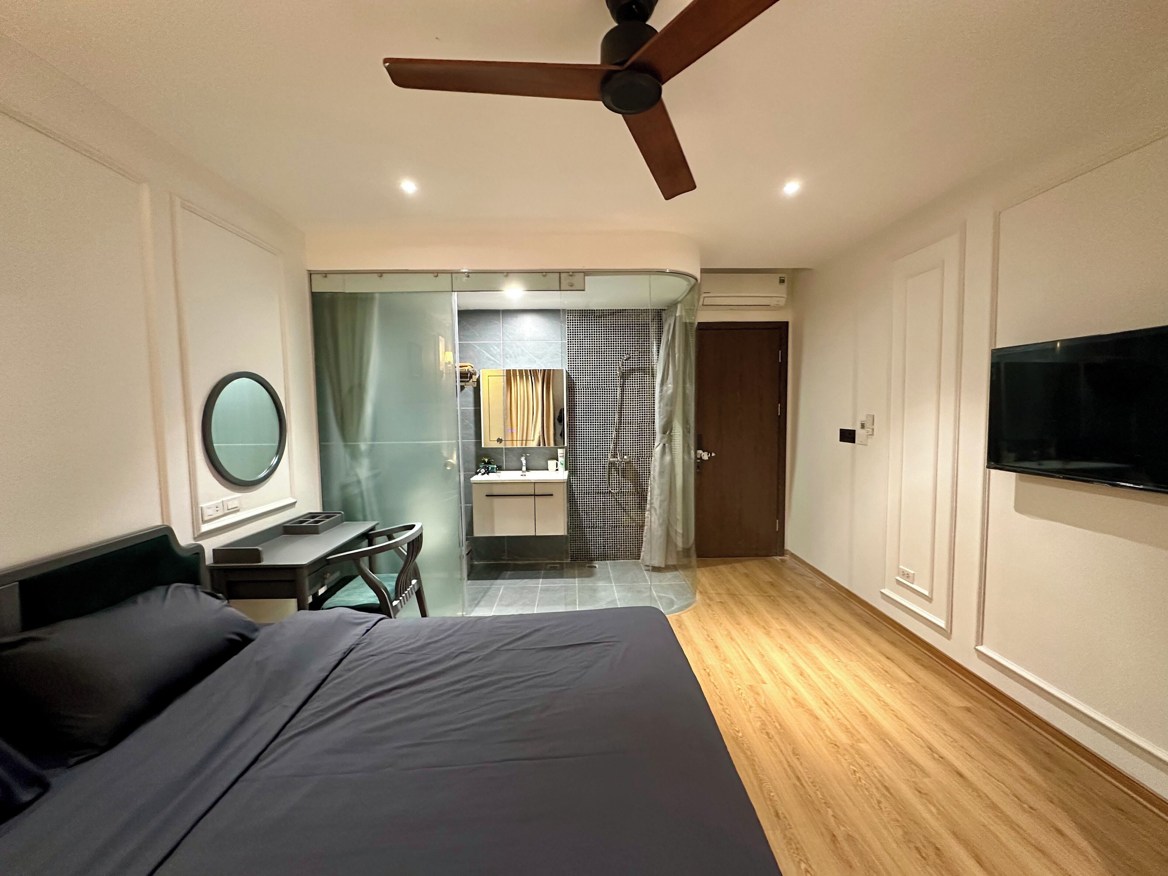 Habitación de hotel con cama, escritorio, espejo, televisor y zona de ducha.