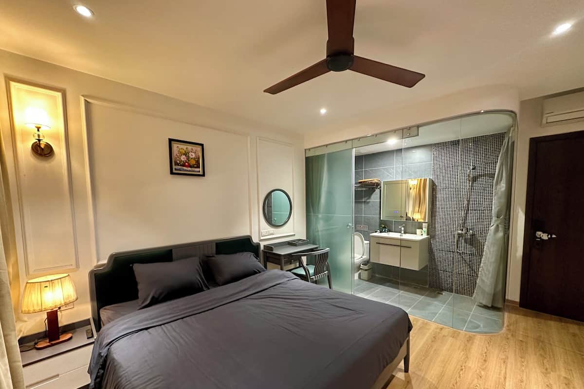 A modern hotel room with a bed, bedside table, lamp, and a view into the bathroom.