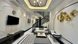 A modern living room with a flat-screen TV, a staircase, and a decorative wall piece. - Bay Luxury Villa OCP2 - Self Checkin (Nghia Tru)