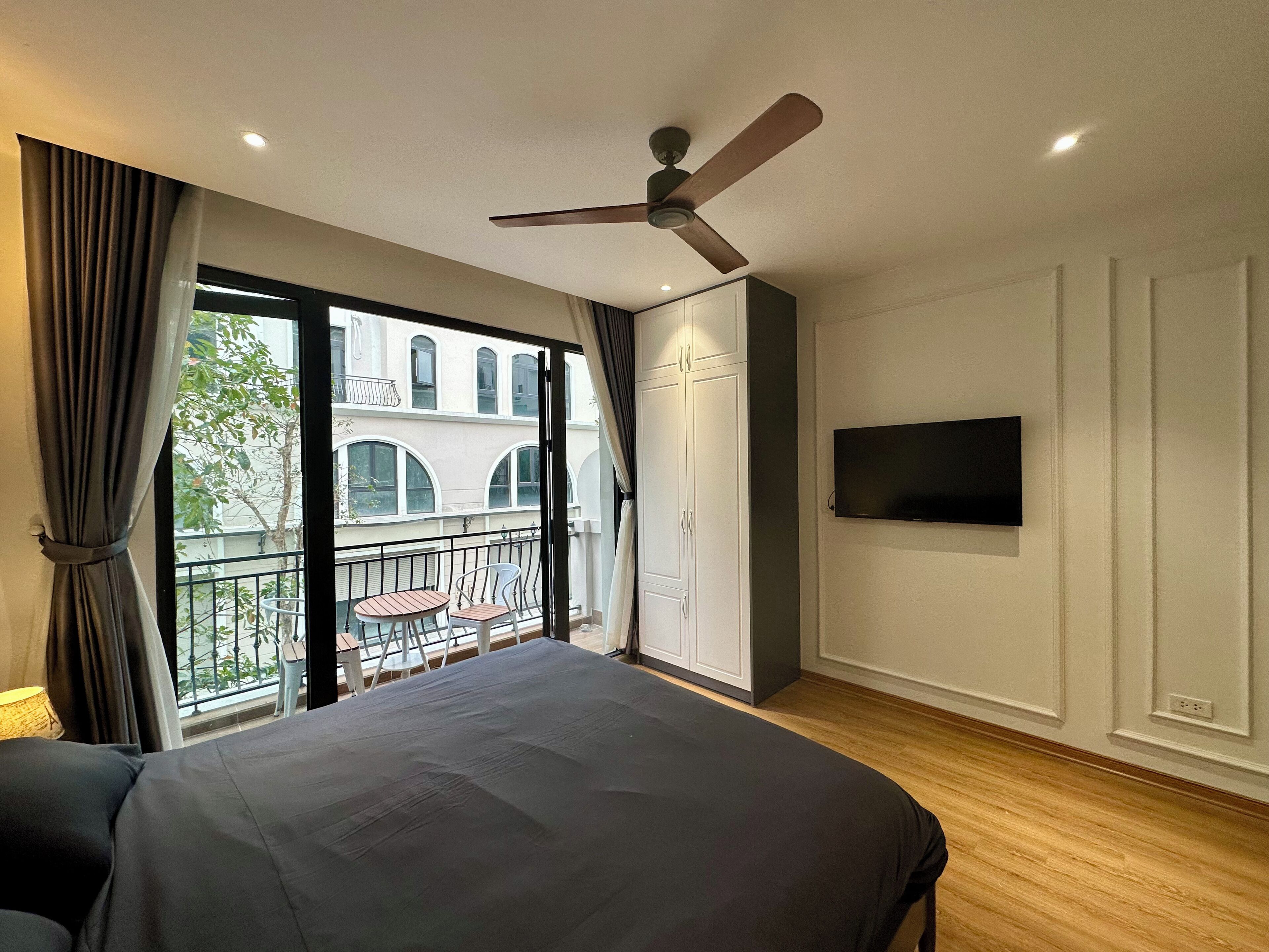 Un dormitorio con cama, ventilador de techo, televisión y balcón con mesa y sillas.