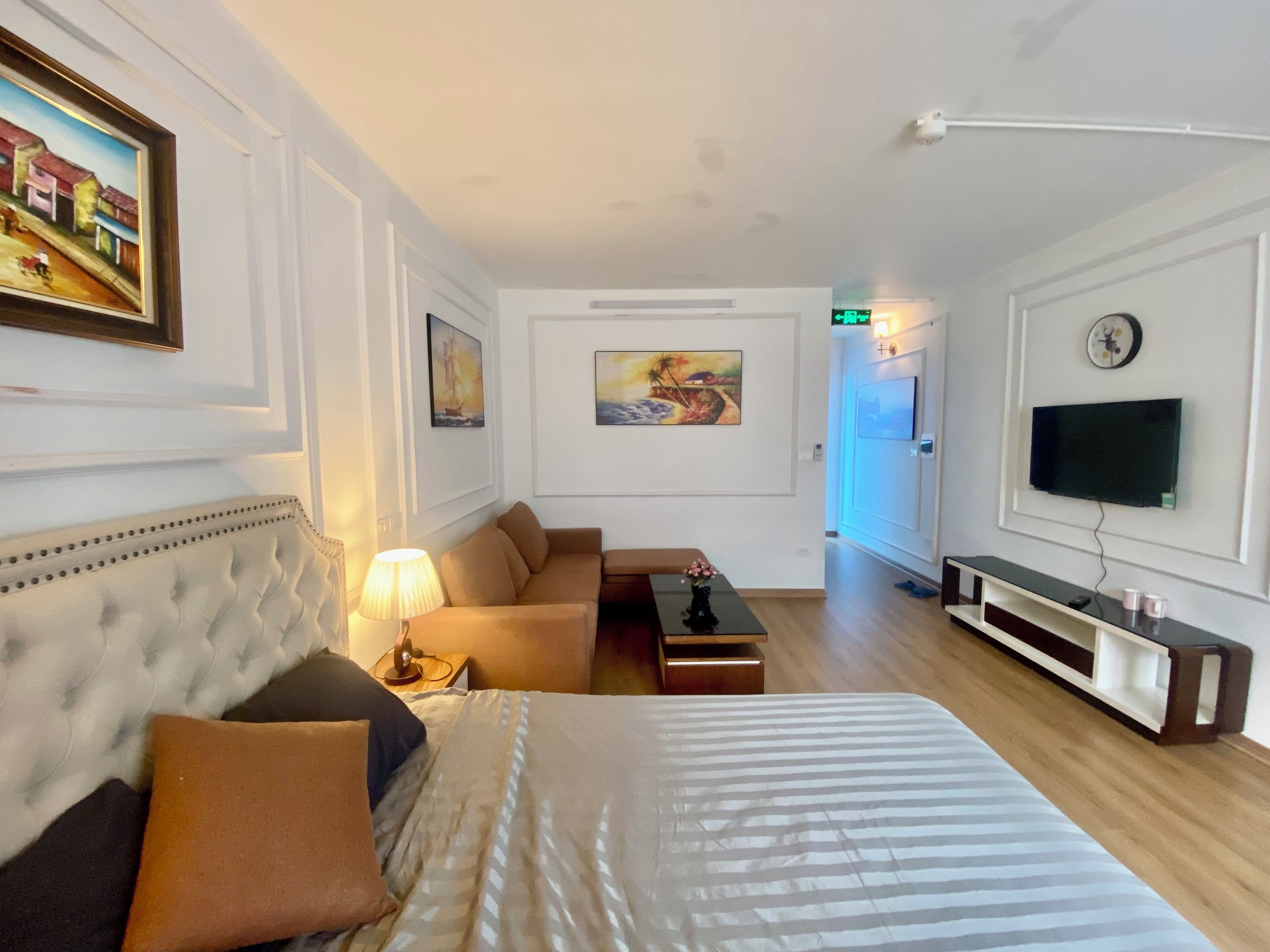 Une chambre d’hôtel avec un grand lit, un canapé, une télévision et des œuvres d’art accrochées aux murs.