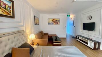 A hotel room with a large bed, a sofa, a TV, and artwork on the walls.