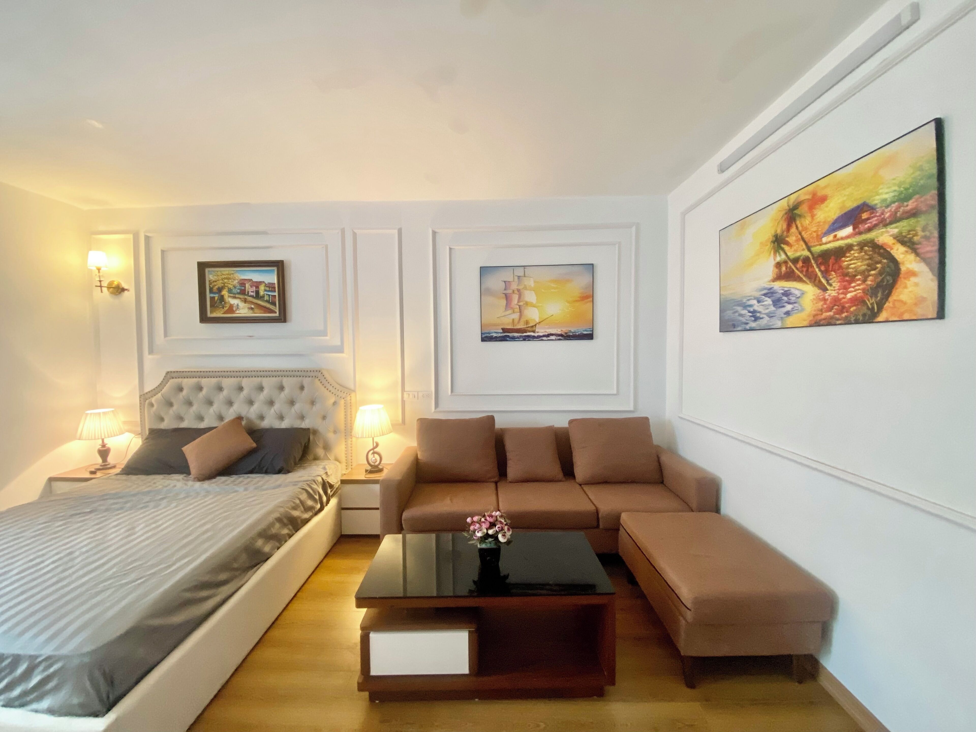 A hotel room with a bed, a sofa, a coffee table, and artwork on the walls.
