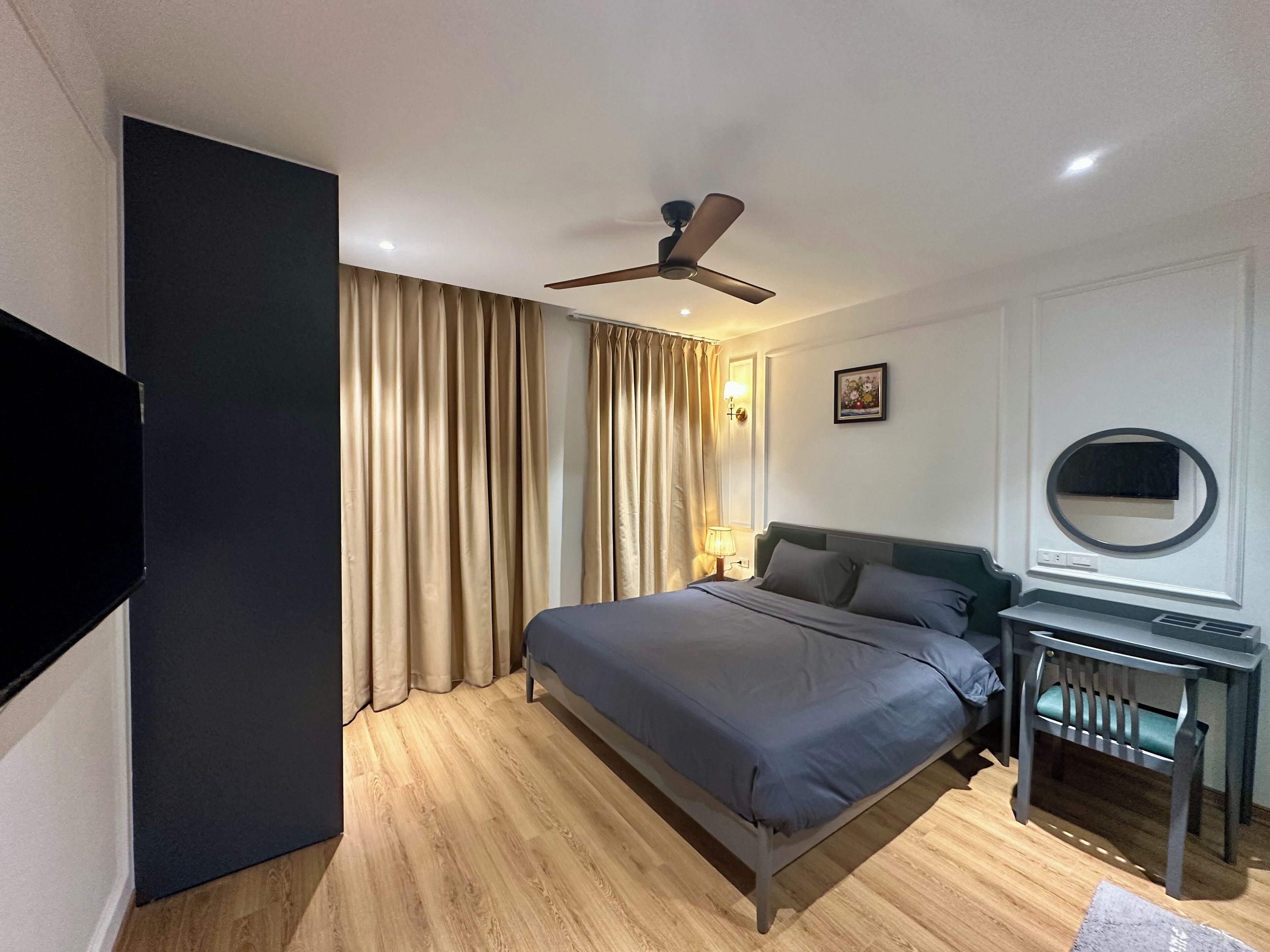 A hotel room with a bed, a desk, a chair, a ceiling fan, and a television.