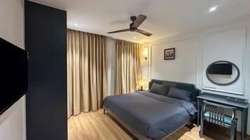 A hotel room with a bed, a desk, a chair, a ceiling fan, and a television.