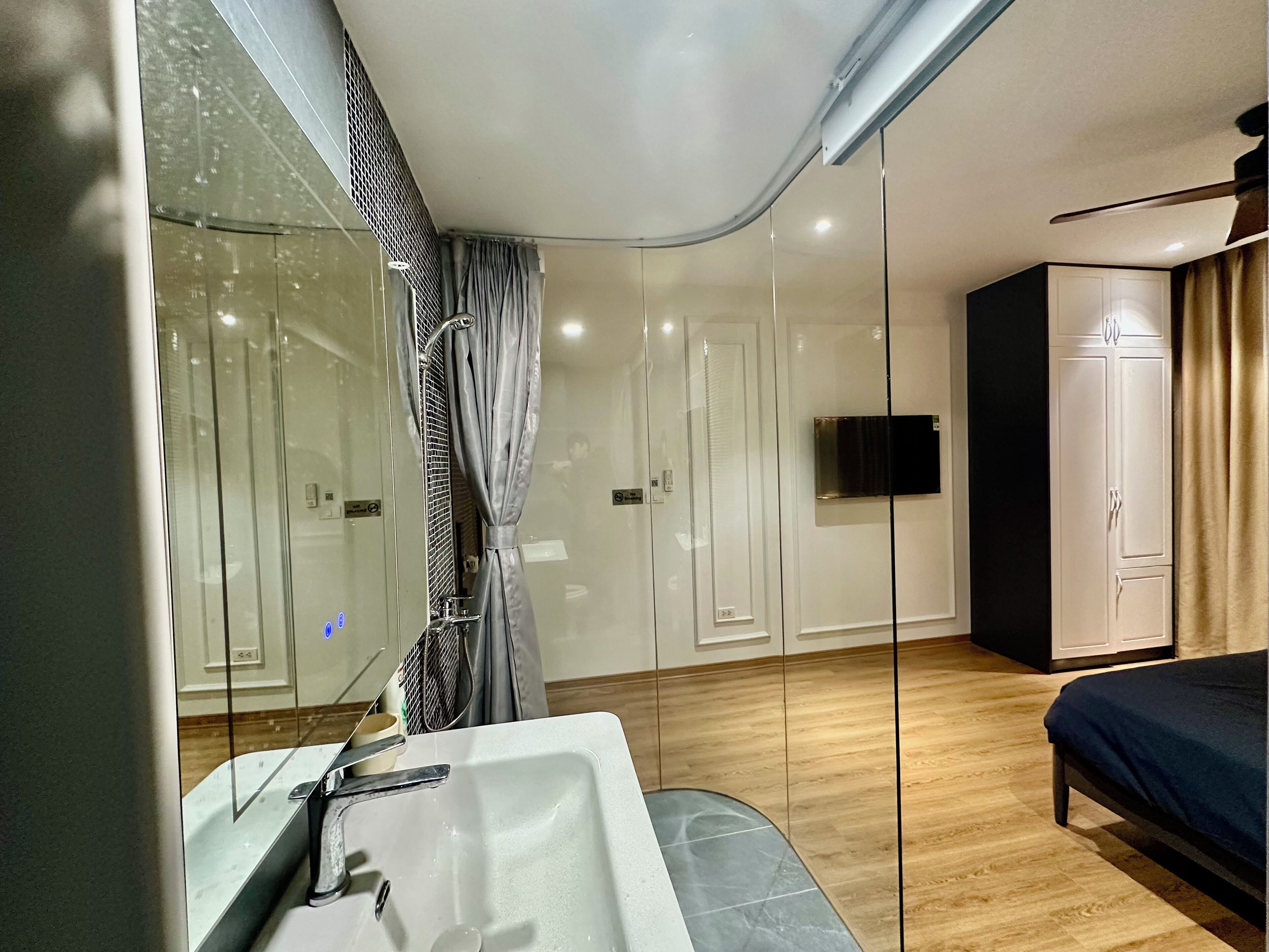 A modern bedroom with a large bed, a built-in TV, and a glass shower enclosure.