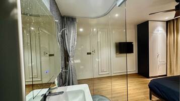 A modern bedroom with a large bed, a built-in TV, and a glass shower enclosure.