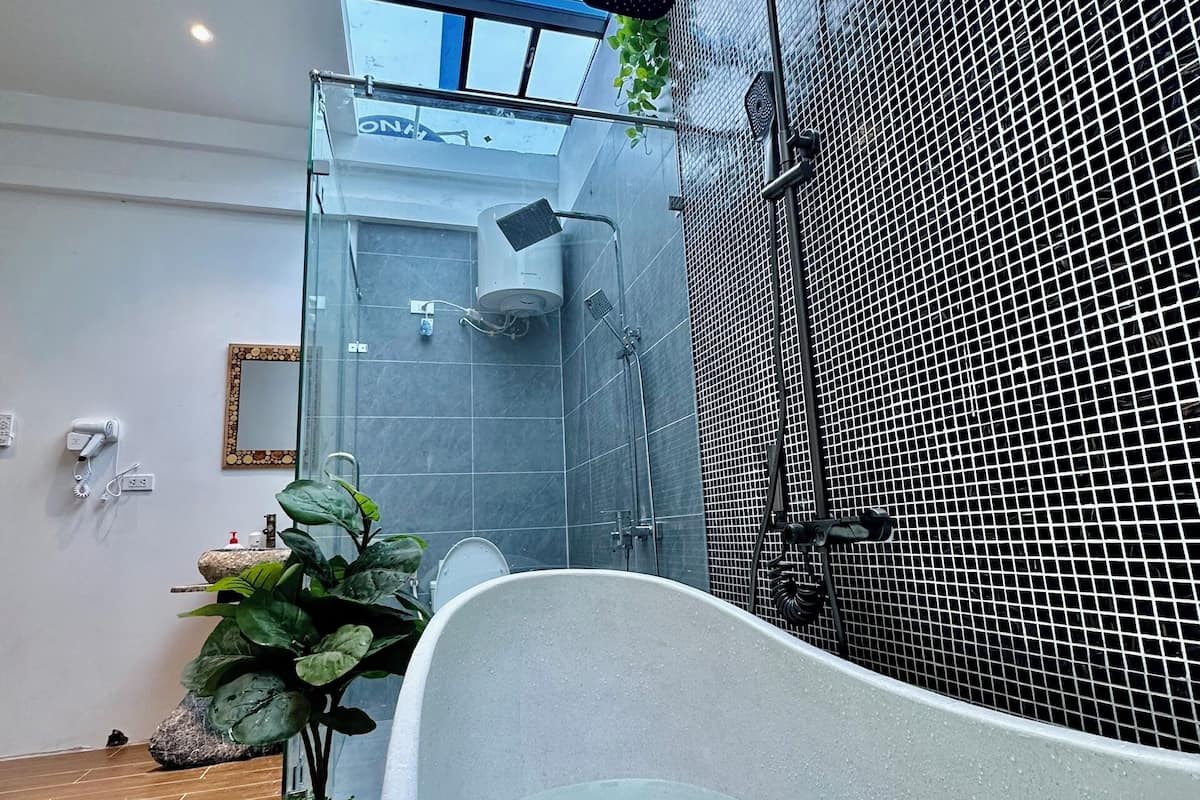 A modern bathroom with a freestanding bathtub, a glass shower enclosure, and a potted plant.