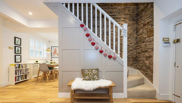 A staircase with a stone wall, a white bench with a fur throw, and a bookshelf with books.