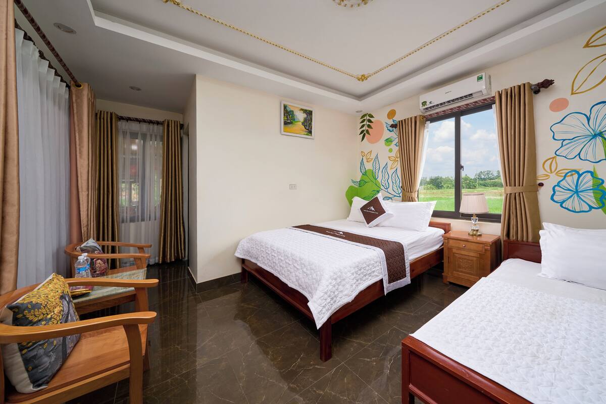 A hotel room with two beds, a wooden chair, a small table, and a window with curtains.