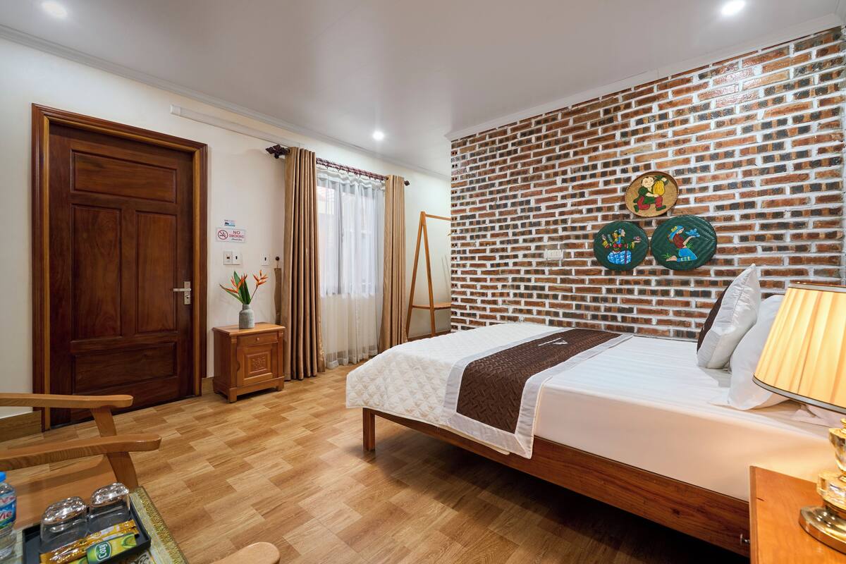 A hotel room with a wooden bed, a brick-patterned wall, and a small table with a lamp.
