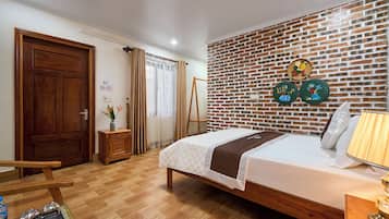 A hotel room with a wooden bed, a brick-patterned wall, and a small table with a lamp.