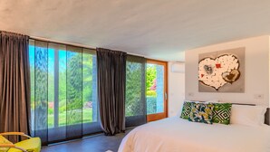 Een moderne slaapkamer met een groot bed, een groene stoel en uitzicht op een tuin door middel van schuifdeuren.