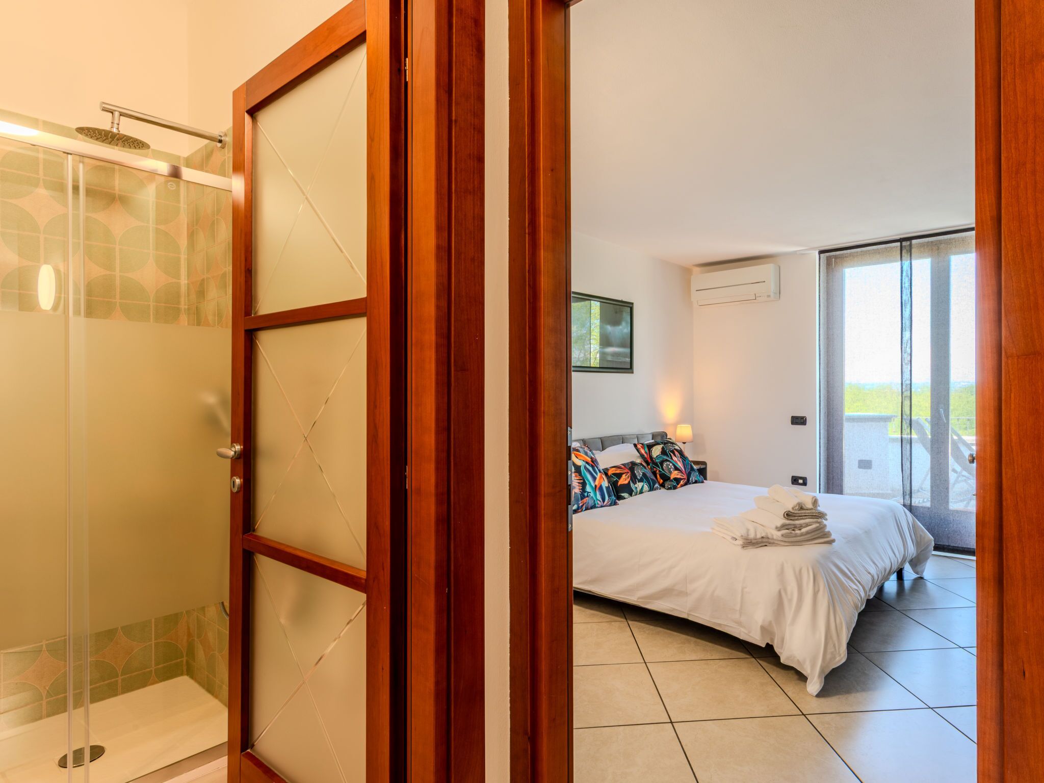 A hotel room with a shower, a bed with colorful pillows, and a view of the outdoors.