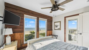 A bedroom with a bed, a ceiling fan, a TV mounted on the wall, and a view of the beach. - Stunning Beach Front Paradise (Surfside Beach)