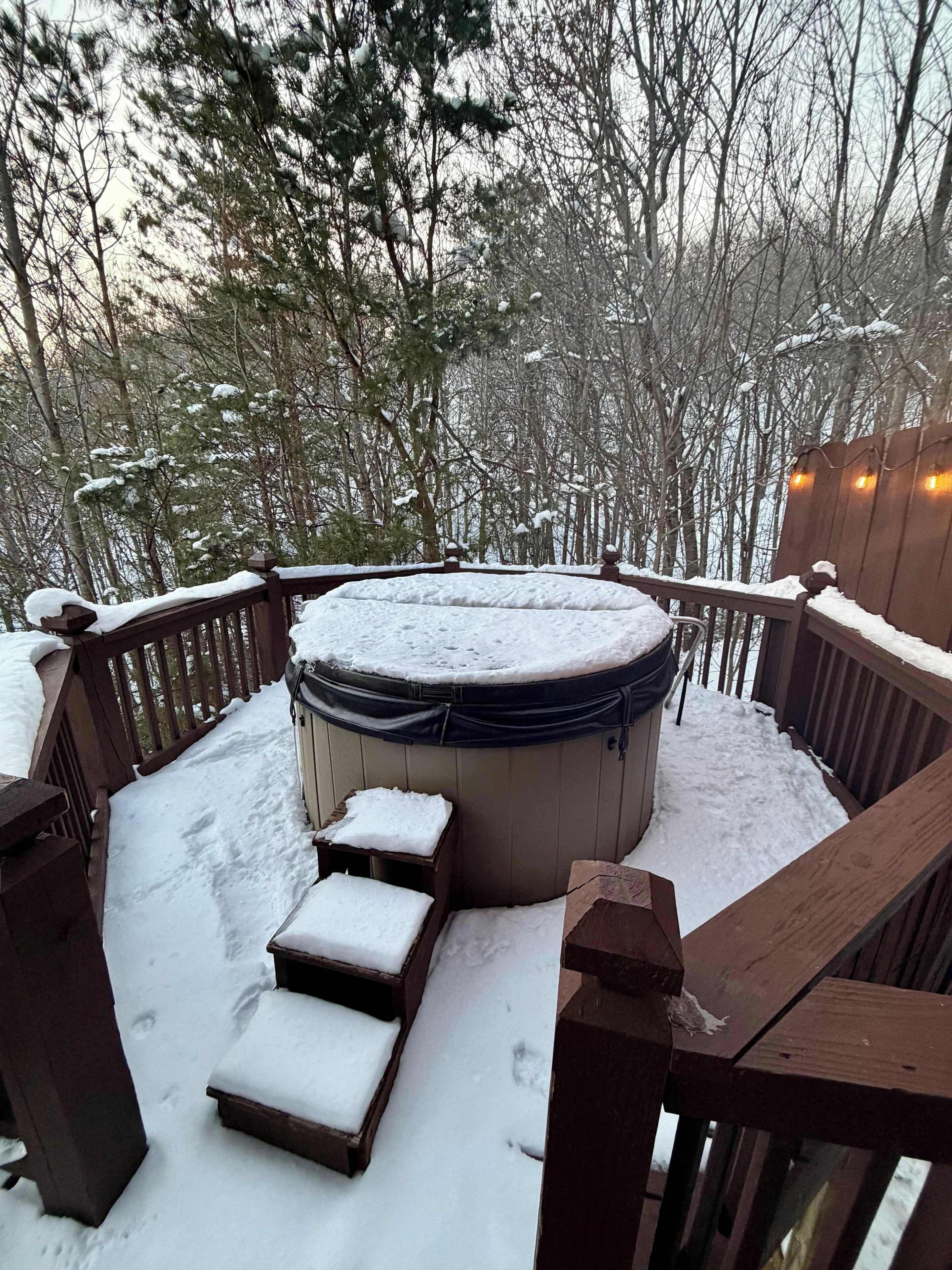 Eine Holzterrasse mit Whirlpool, umgeben von Schnee, Holzetagen und einem Geländer.