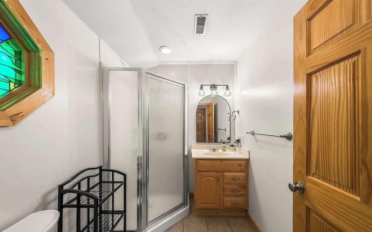 Une salle de bain compacte avec une douche à parois de verre, un meuble-lavabo en bois avec un miroir et des toilettes blanches.